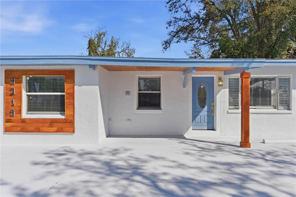 A white house exterior features a blue front door, wood accents, and a covered porch — 9315 N 16TH STREET, TAMPA, FL