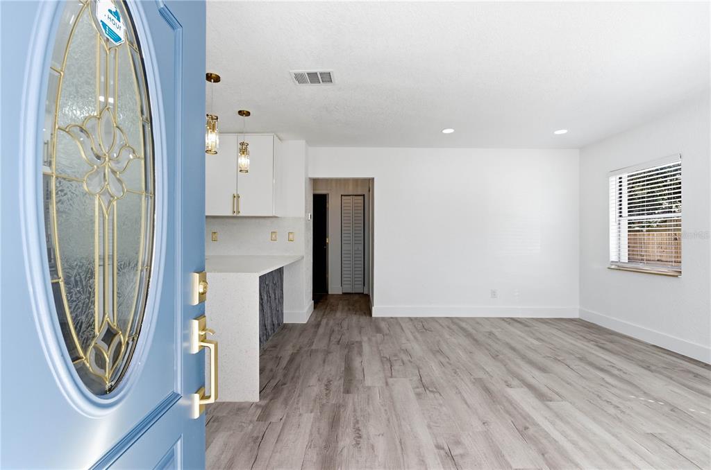 A view from a blue front door into an open-concept living area with wood-look flooring — 9315 N 16TH STREET, TAMPA, FL