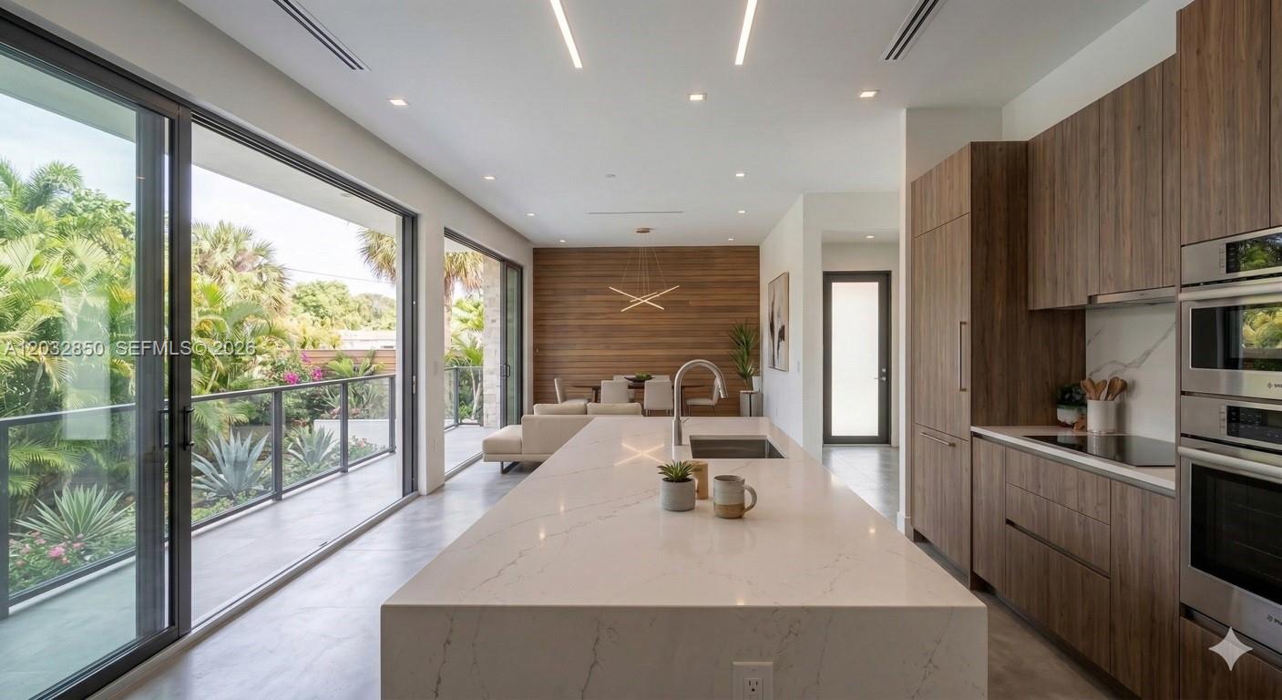 A modern kitchen features a large white quartz island, wood cabinetry, and floor-to-ceiling glass doors — 5650 N Miami Ave, Miami FL 33127, MIAMI, FL