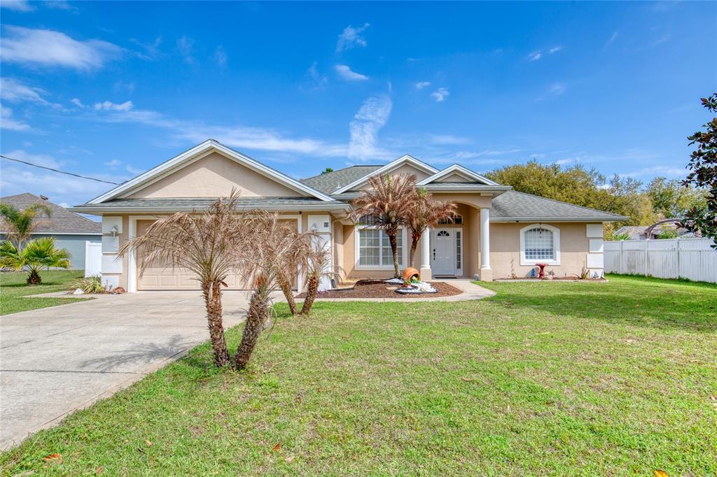 A single-story tan house with a two-car garage, front lawn, and palm trees — 89 FELWOOD LANE, PALM COAST, FL