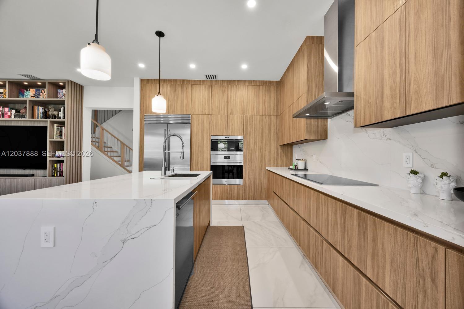 A modern kitchen features wood cabinetry, a white marble island, and stainless steel appliances — 12021 SW 82nd Pl, Miami FL 33156, MIAMI, FL