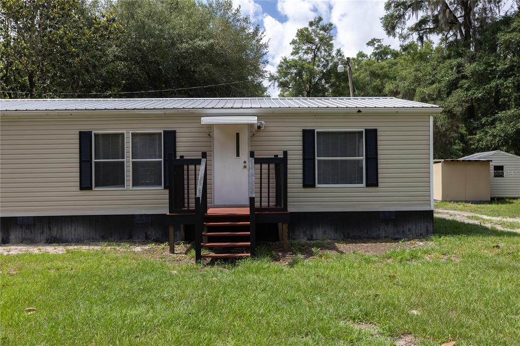 A single-story mobile home with tan siding, black shutters, and a small wooden front porch — 4950 SW 80TH STREET, CHIEFLAND, FL