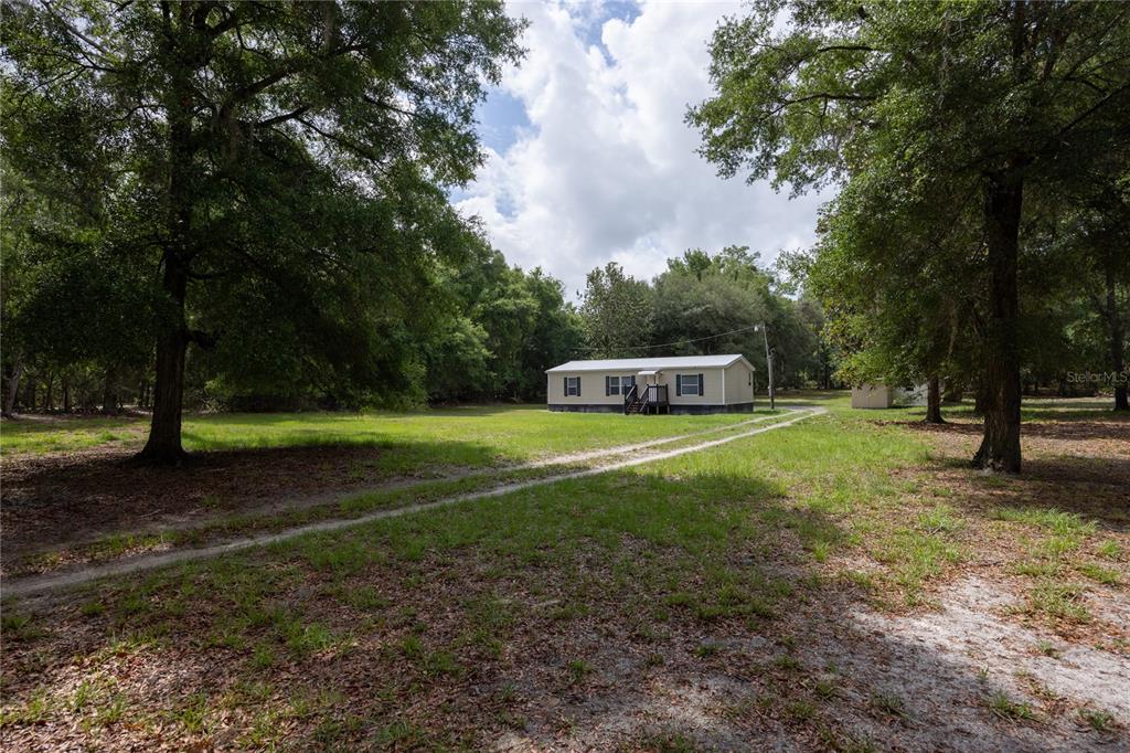 A single-story manufactured home sits on a grassy lot surrounded by mature trees — 4950 SW 80TH STREET, CHIEFLAND, FL