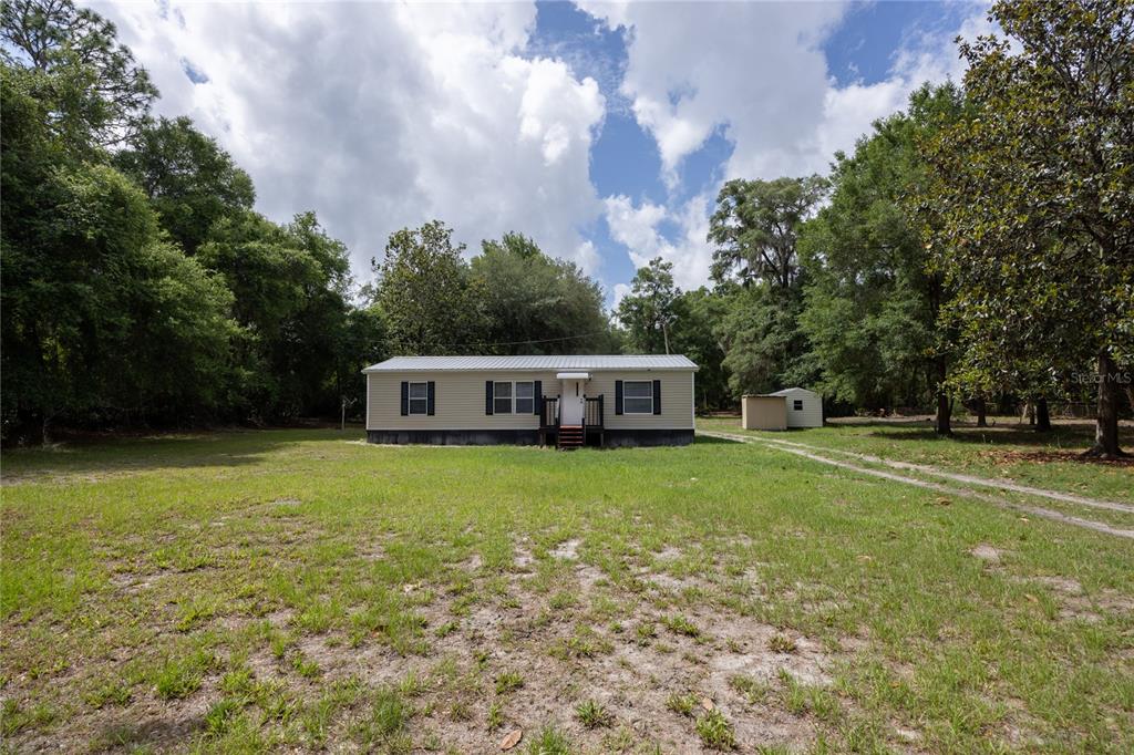 A single-story manufactured home sits on a large, grassy lot surrounded by mature trees — 4950 SW 80TH STREET, CHIEFLAND, FL