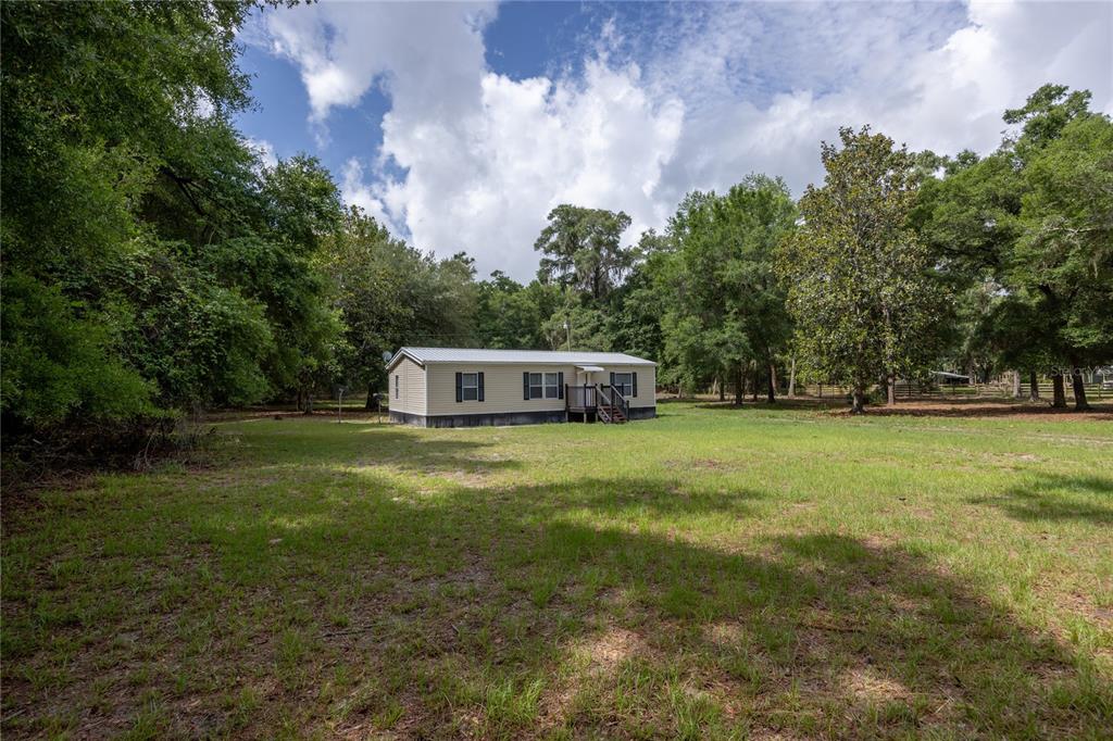 A single-story manufactured home sits in the center of a large, grassy, tree-lined lot — 4950 SW 80TH STREET, CHIEFLAND, FL