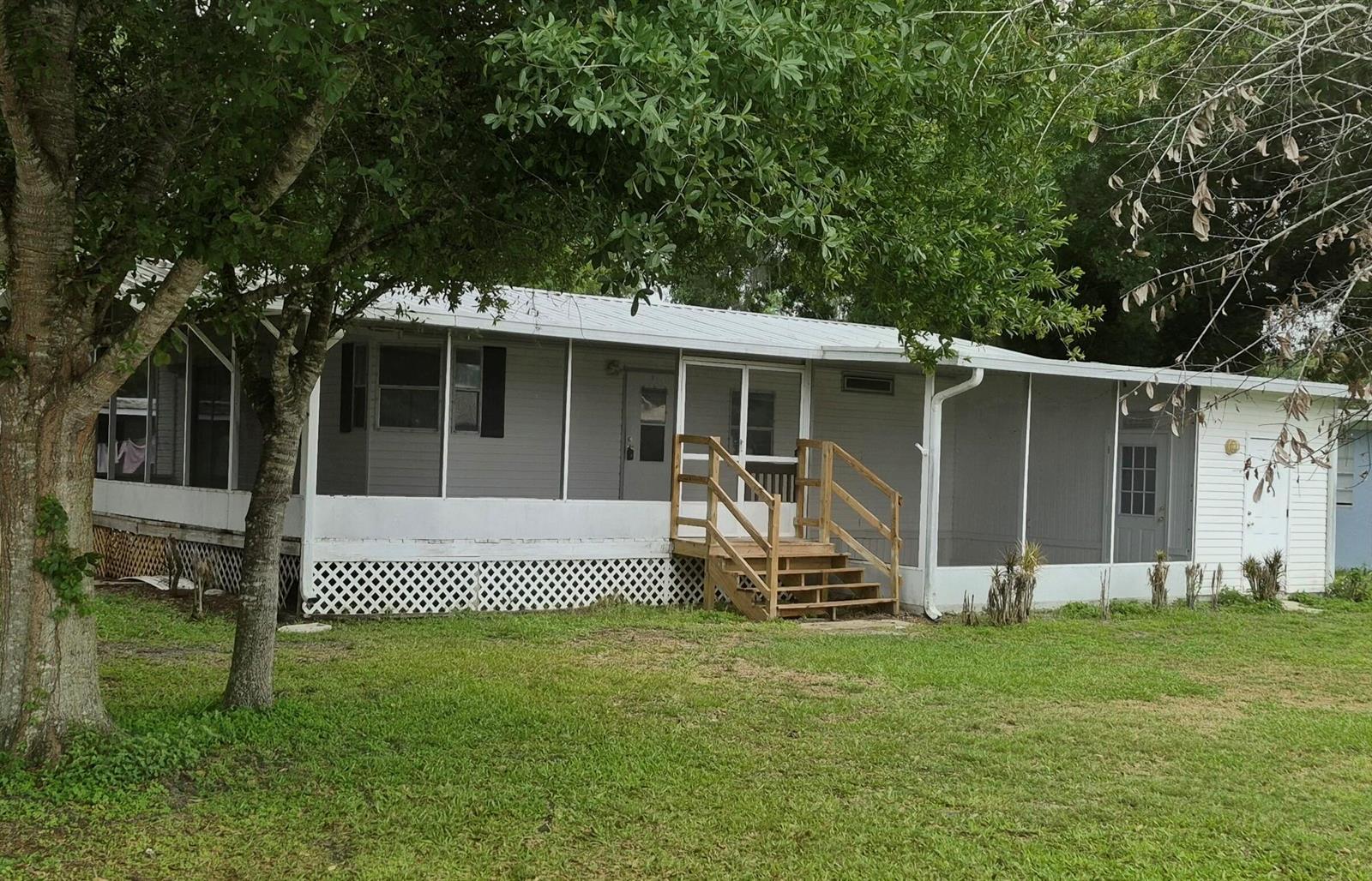 A single-story manufactured home with a screened-in porch and wooden stairs on a grassy lot — 301 SE 5th Avenue, Okeechobee FL 34974, OKEECHOBEE, FL