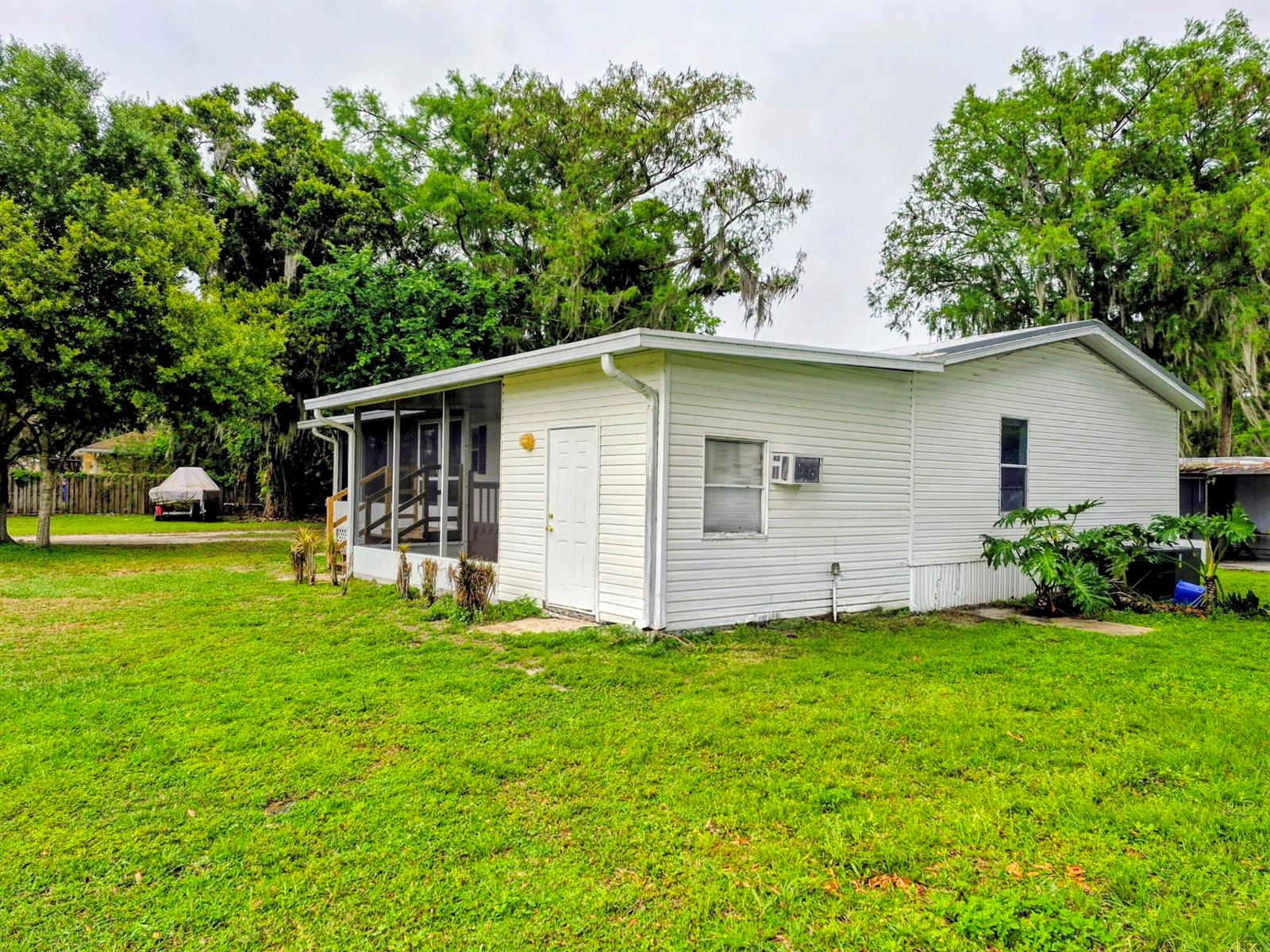 A white single-story house with a screened-in porch stands on a grassy lawn — 301 SE 5th Avenue, Okeechobee FL 34974, OKEECHOBEE, FL