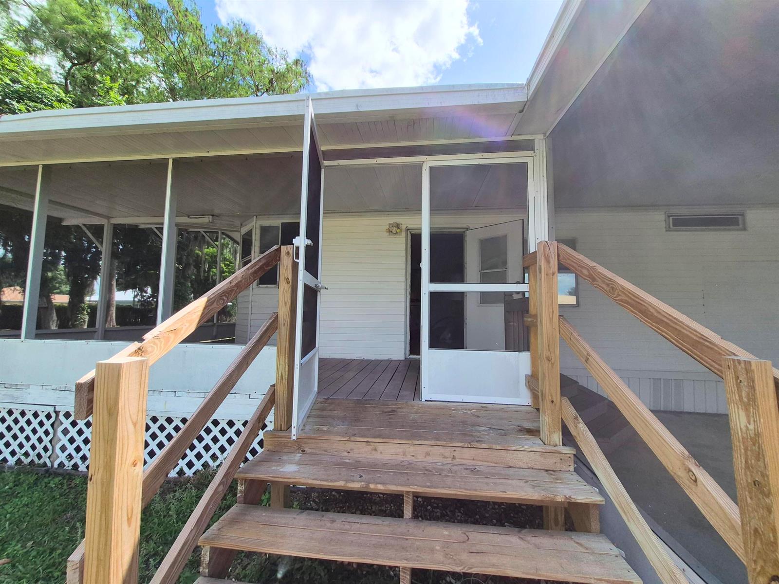 A wooden staircase leads to a screened-in porch entrance of a white mobile home — 301 SE 5th Avenue, Okeechobee FL 34974, OKEECHOBEE, FL