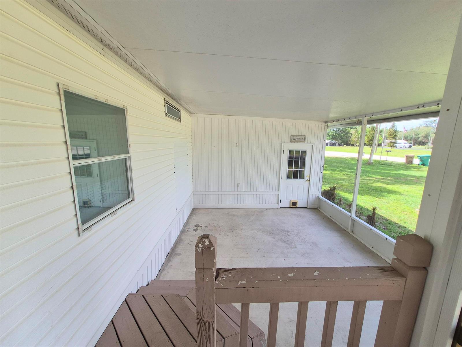 A covered screened-in porch with white siding, a concrete floor, and wooden stairs — 301 SE 5th Avenue, Okeechobee FL 34974, OKEECHOBEE, FL