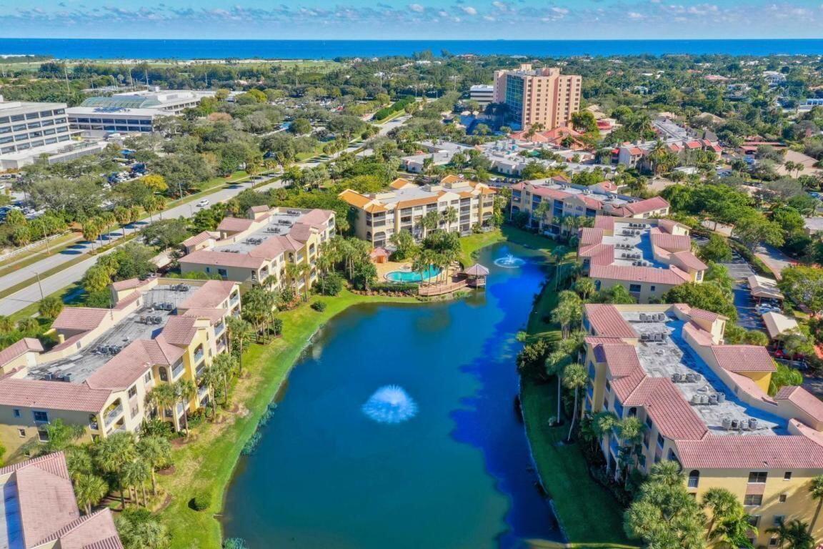 An aerial view of a multi-building apartment complex surrounding a lake with a central fountain — 400 Uno Lago Drive # 103, Juno Beach FL 33408, JUNO BEACH, FL