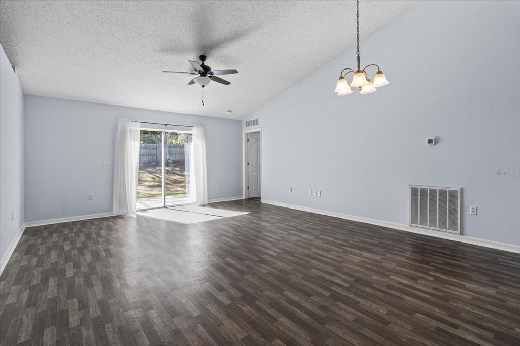 A living room features light blue walls, dark wood-look flooring, a ceiling fan, and sliding doors — 7895 N SARAZEN DRIVE, CITRUS SPRINGS, FL