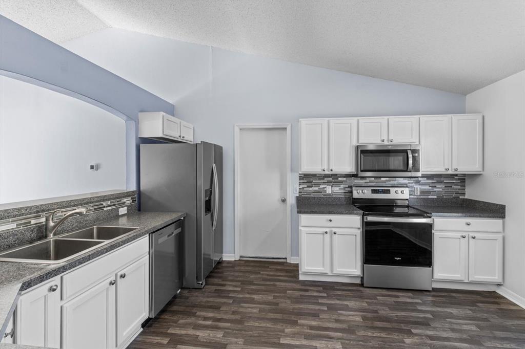 A kitchen features white cabinets, stainless steel appliances, dark countertops, and wood-look flooring — 7895 N SARAZEN DRIVE, CITRUS SPRINGS, FL