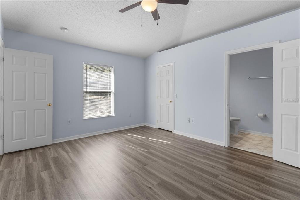 An empty bedroom features light blue walls, wood-look flooring, a ceiling fan, and an attached bathroom — 7895 N SARAZEN DRIVE, CITRUS SPRINGS, FL