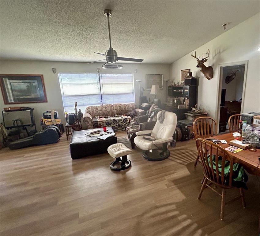 A living room with wood-look flooring, a ceiling fan, a floral sofa, and a deer mount — 2293 BELEN DRIVE, DELTONA, FL