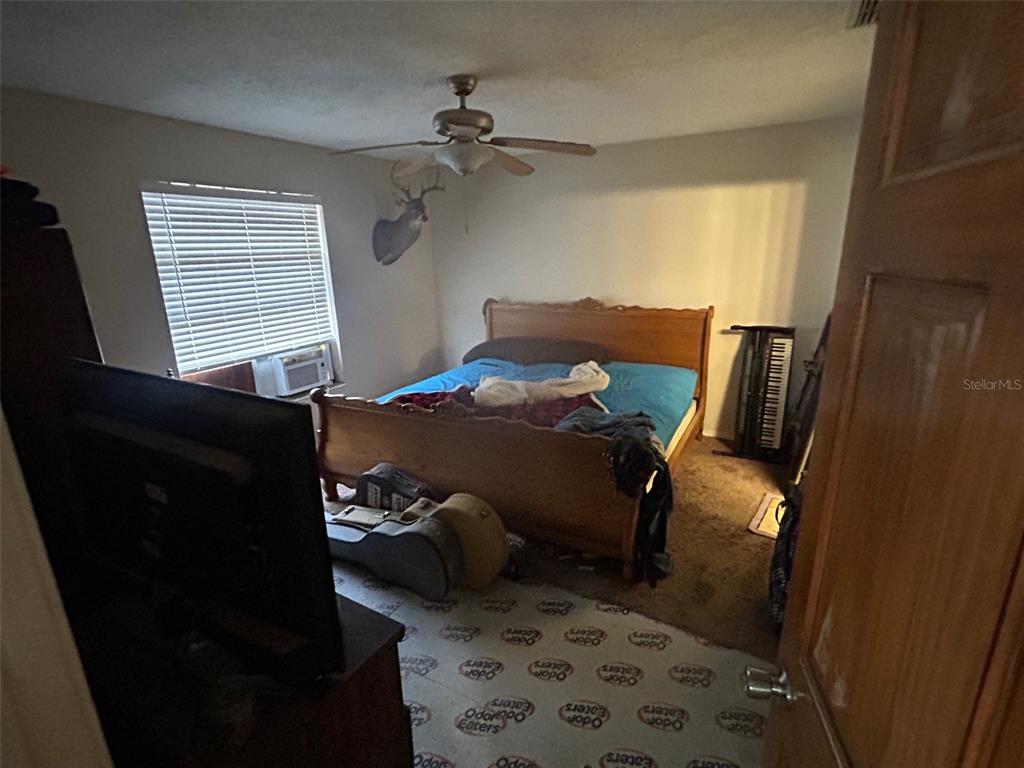 A bedroom features a wooden bed frame, a ceiling fan, a deer mount, and carpeted flooring — 2293 BELEN DRIVE, DELTONA, FL
