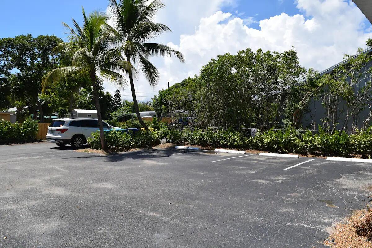 An asphalt parking lot with marked spaces sits in front of trees and a white vehicle — 523 SE 20th Court # 5, Boynton Beach FL 33435, BOYNTON BEACH, FL