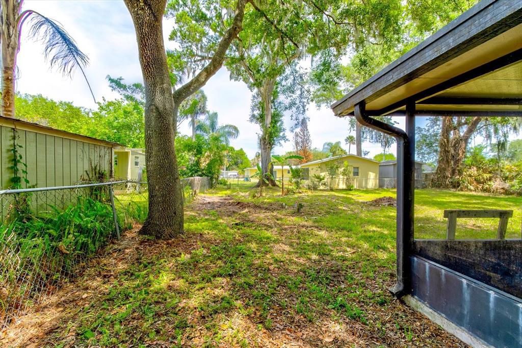 A grassy backyard features mature trees, a chain-link fence, and a screened-in porch area — 113 FRAN DRIVE, NEW SMYRNA BEACH, FL