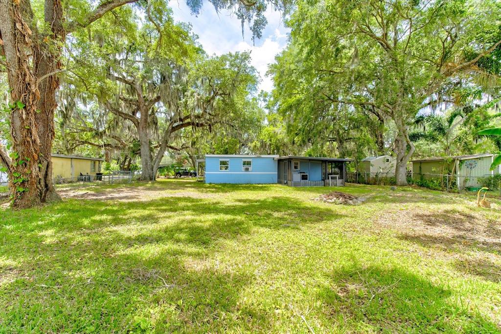 A blue mobile home sits in a grassy yard surrounded by large, moss-draped oak trees — 113 FRAN DRIVE, NEW SMYRNA BEACH, FL