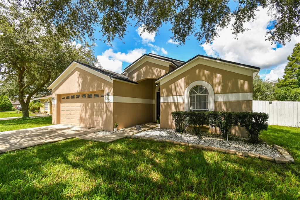 A tan single-story house with a two-car garage, arched window, and a landscaped front yard — 24541 LAUREL RIDGE DRIVE, LUTZ, FL