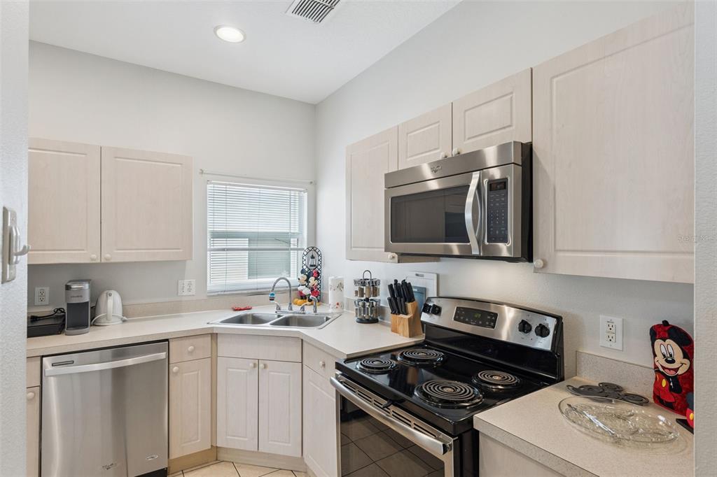 A kitchen features light wood cabinets, stainless steel appliances, and a corner sink — 8152 SUN PALM DRIVE, KISSIMMEE, FL
