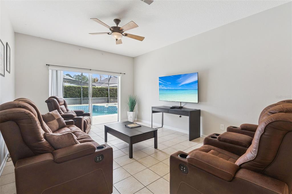 A living room with brown reclining furniture, a coffee table, and a sliding door to a pool — 8152 SUN PALM DRIVE, KISSIMMEE, FL