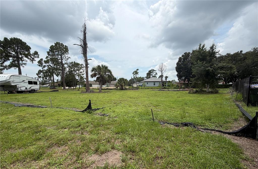 A grassy, vacant residential lot features a parked camper, scattered trees, and a perimeter fence — RASP COURT, NORTH PORT, FL