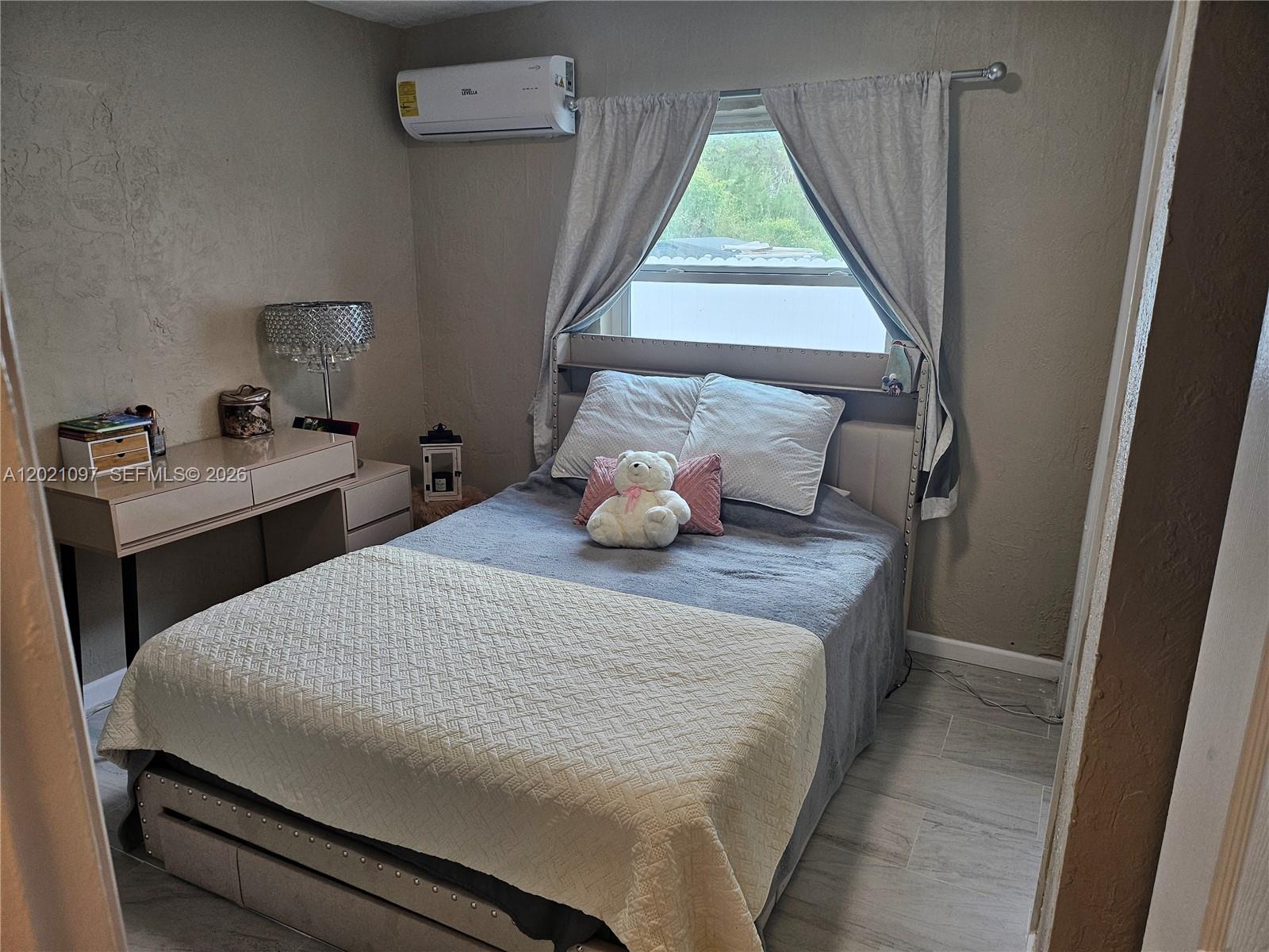 A bedroom features a bed with a gray quilt, a desk, and a wall-mounted air conditioner — 528 NW 10th St, Florida City FL 33034, FLORIDA CITY, FL