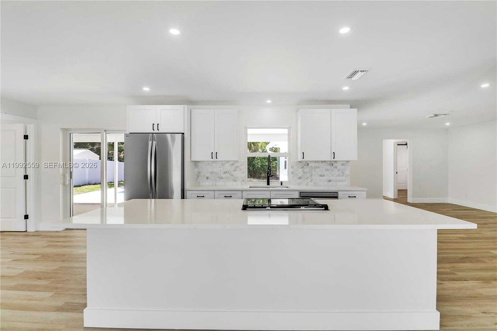 A modern kitchen features white cabinetry, a large center island, and light wood flooring — 404 Highwood Circle, Jupiter FL 33458, JUPITER, FL