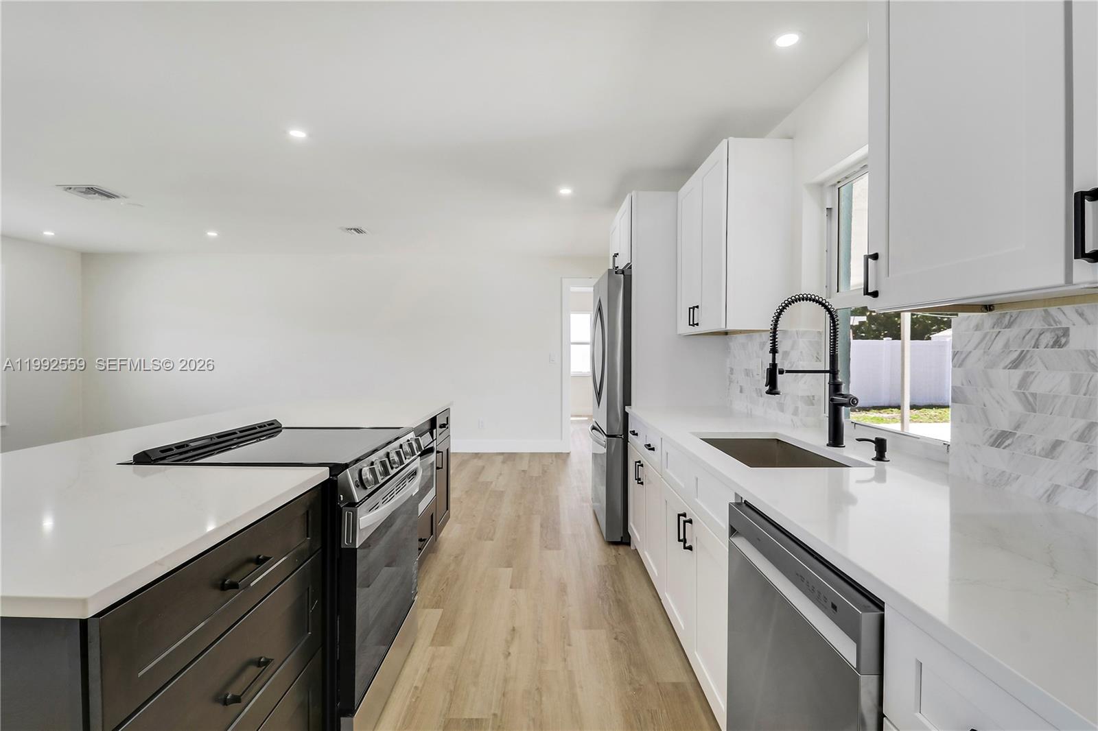 A modern kitchen features white cabinets, dark lower island cabinetry, and stainless steel appliances — 404 Highwood Circle, Jupiter FL 33458, JUPITER, FL