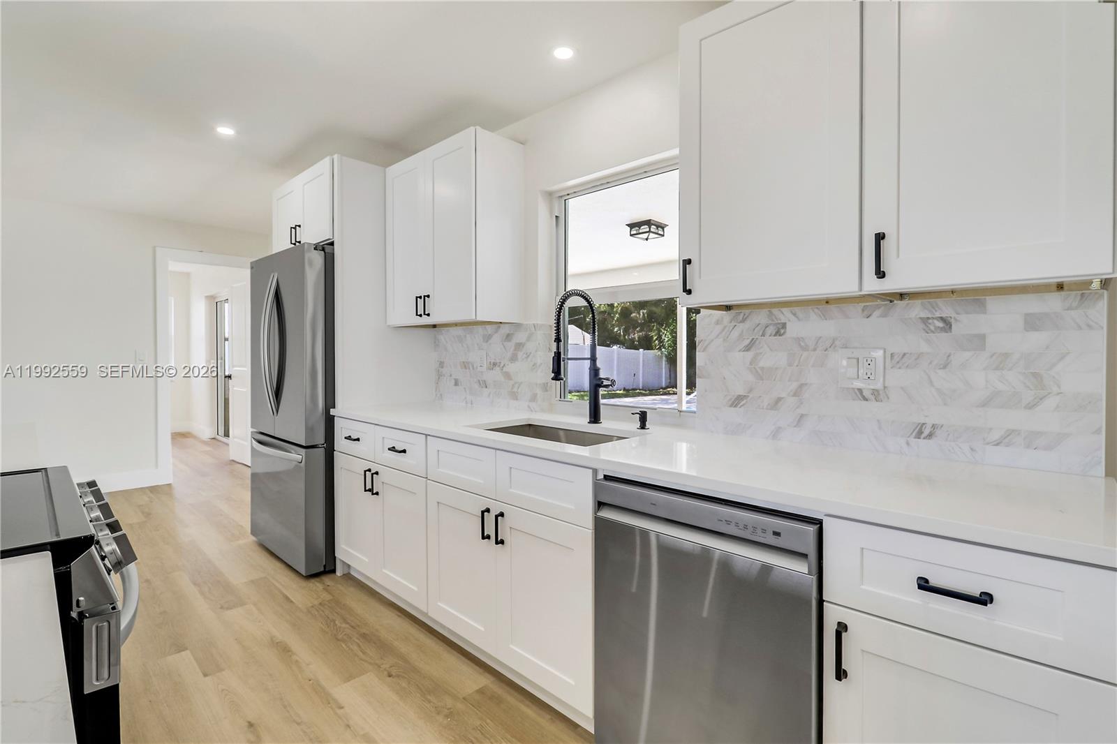 A modern kitchen features white cabinets, stainless steel appliances, and a marble herringbone backsplash — 404 Highwood Circle, Jupiter FL 33458, JUPITER, FL