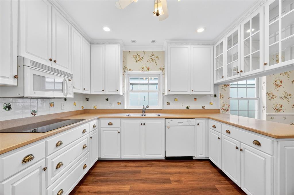A kitchen features white cabinets, tan countertops, floral wallpaper, and wood-look flooring — 5941 CHESAPEAKE PARK UNIT GE, ORLANDO, FL