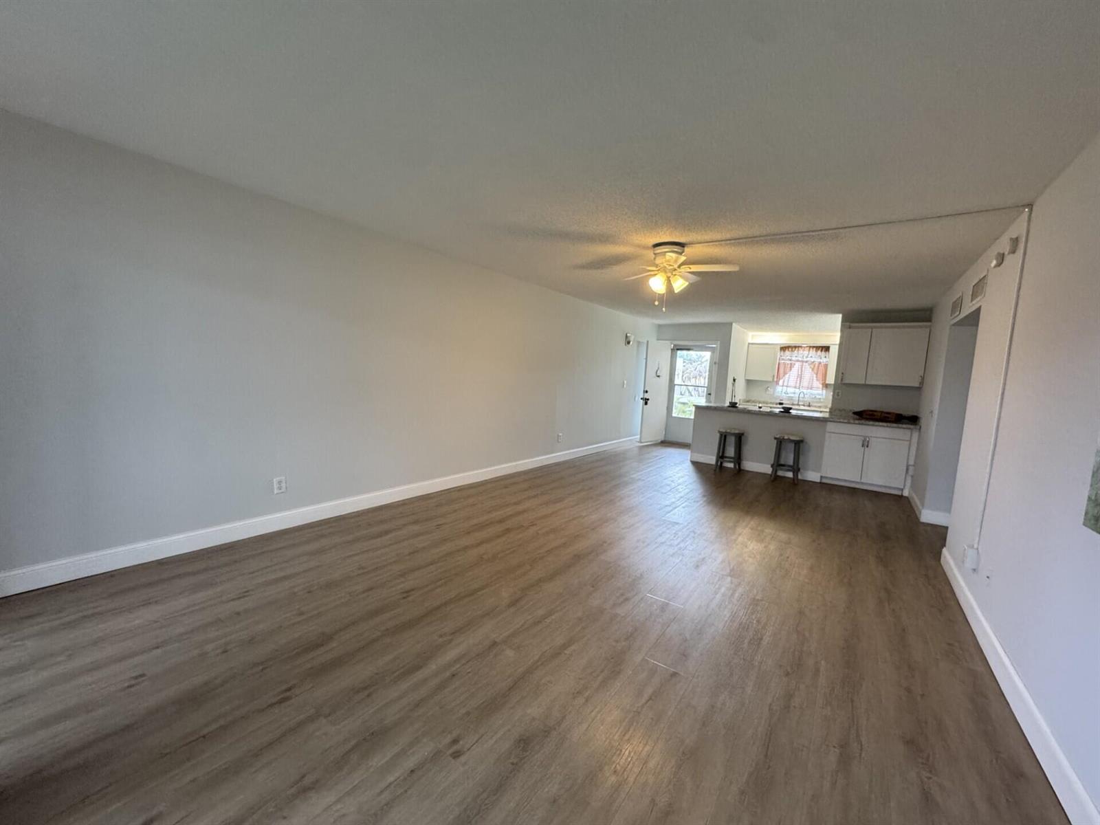 An open-concept living area features light gray walls, wood-look flooring, and a kitchen breakfast bar — 1310 NE 14th Court Apt K19, Jensen Beach FL 34957, JENSEN BEACH, FL