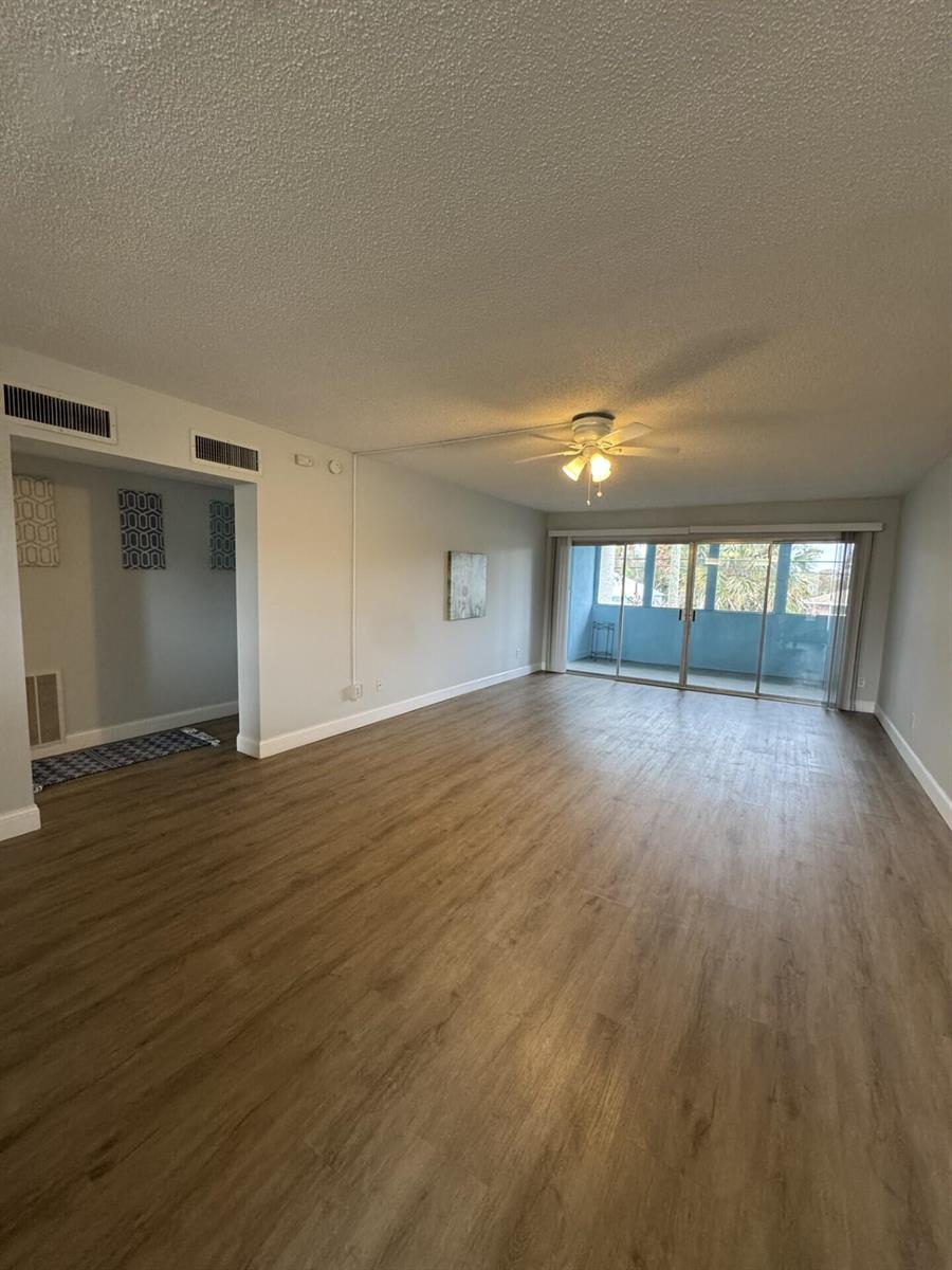 An empty living room features light wood-look flooring, a ceiling fan, and a sliding glass door — 1310 NE 14th Court Apt K19, Jensen Beach FL 34957, JENSEN BEACH, FL