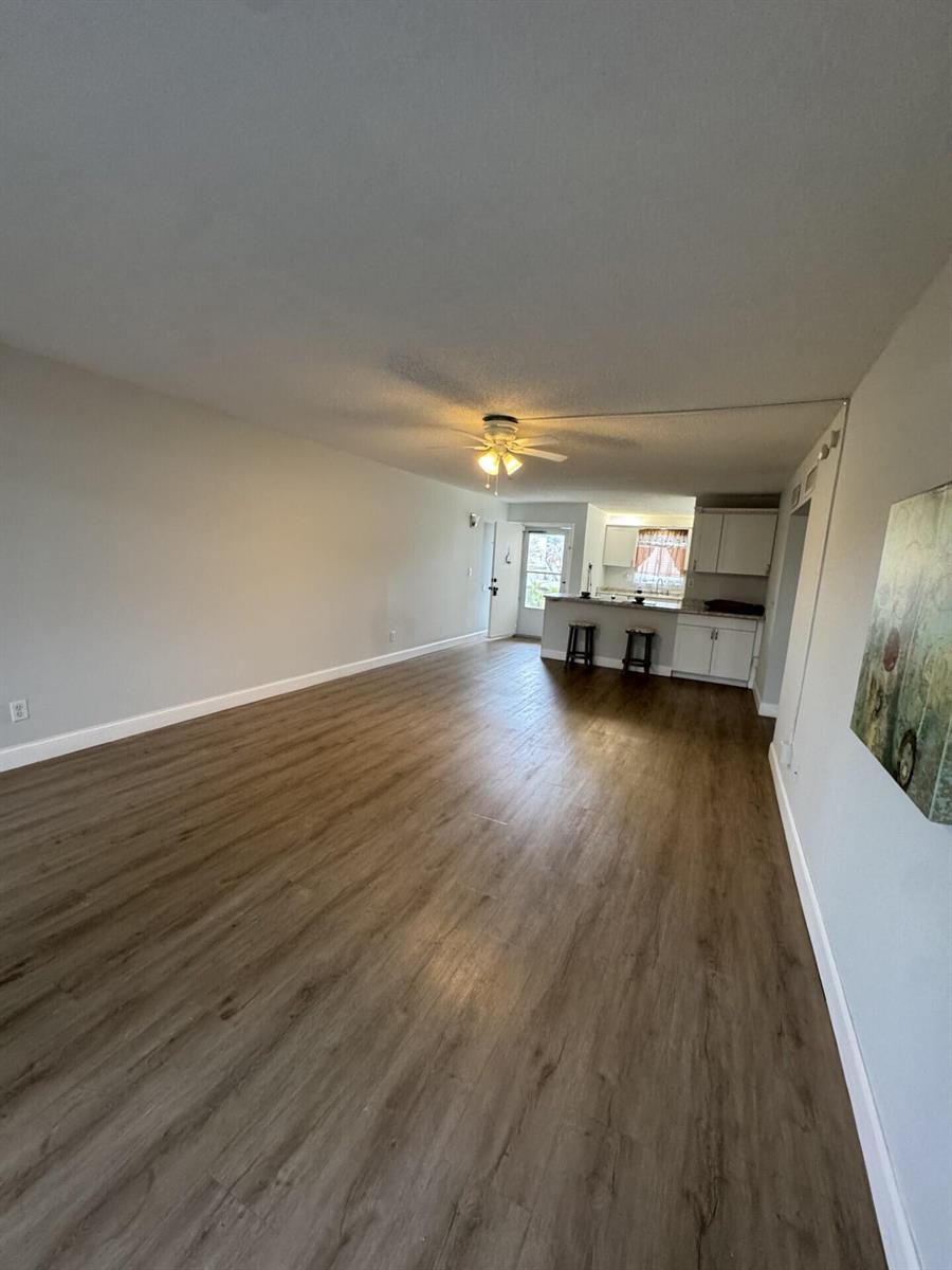 An open-concept living area features wood-look flooring, a ceiling fan, and a kitchen with bar seating — 1310 NE 14th Court Apt K19, Jensen Beach FL 34957, JENSEN BEACH, FL