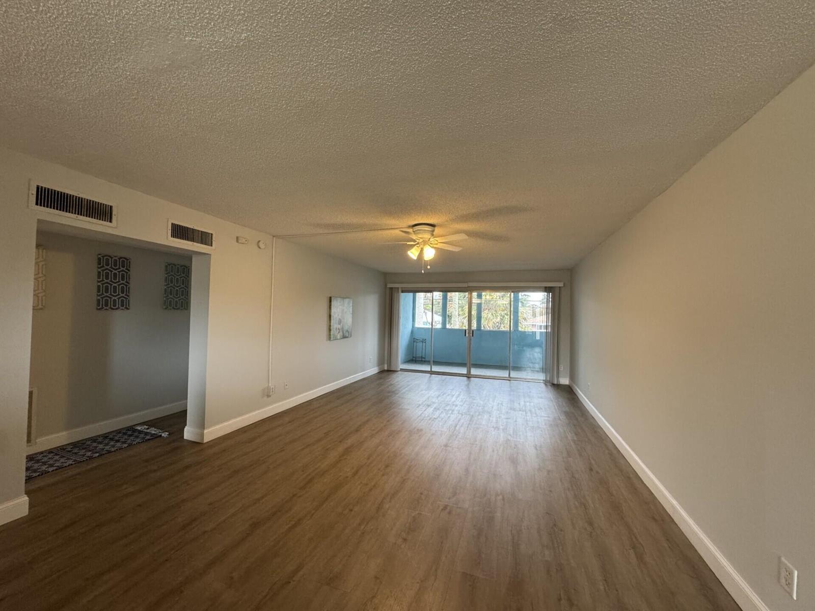 An empty living room features wood-look flooring, a ceiling fan, and sliding glass balcony doors — 1310 NE 14th Court Apt K19, Jensen Beach FL 34957, JENSEN BEACH, FL