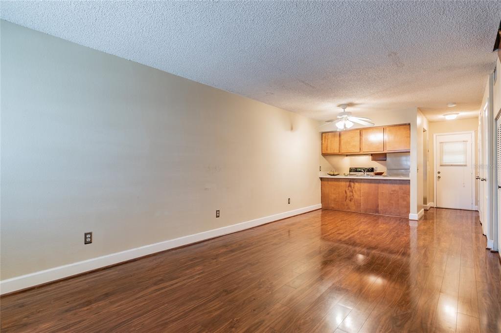 A living room with wood-look flooring and a pass-through kitchen with wood cabinets — 4875 W MCELROY AVENUE UNIT G208, TAMPA, FL