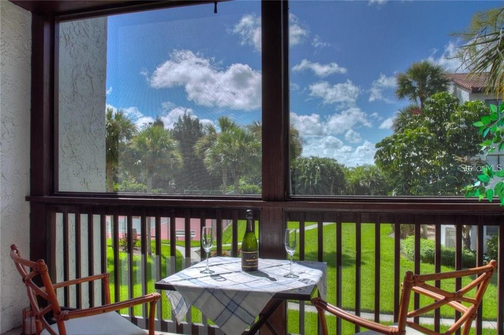 A screened-in balcony features a small table with wine, two chairs, and a tropical view — 1622 STICKNEY POINT ROAD UNIT 22-202, SARASOTA, FL