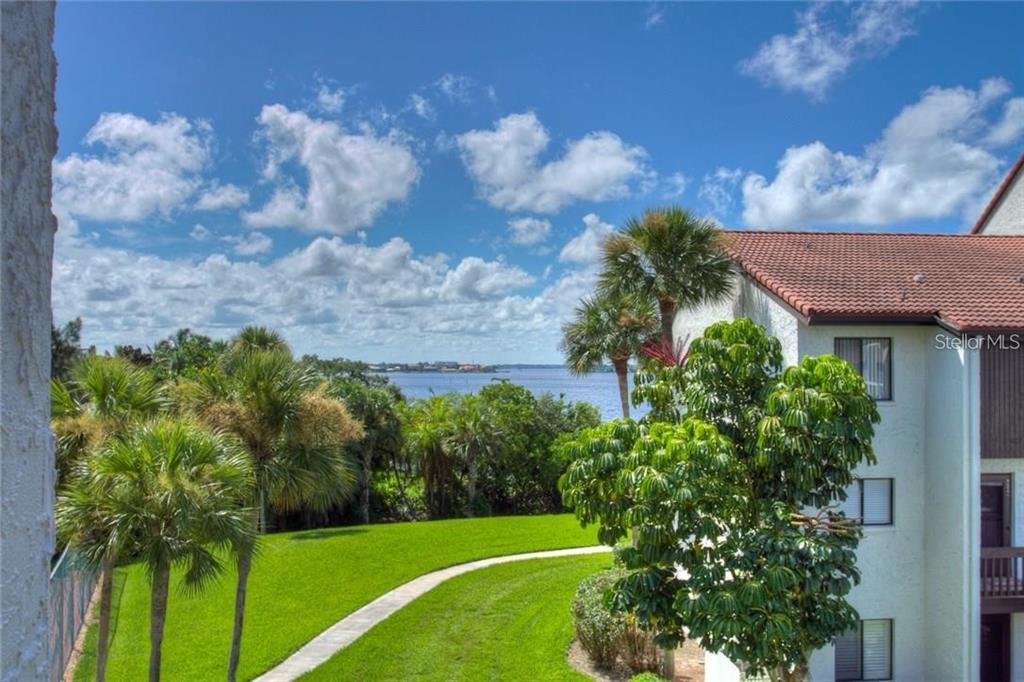 An elevated view of a grassy lawn, palm trees, and a building overlooking a lake — 1622 STICKNEY POINT ROAD UNIT 22-202, SARASOTA, FL