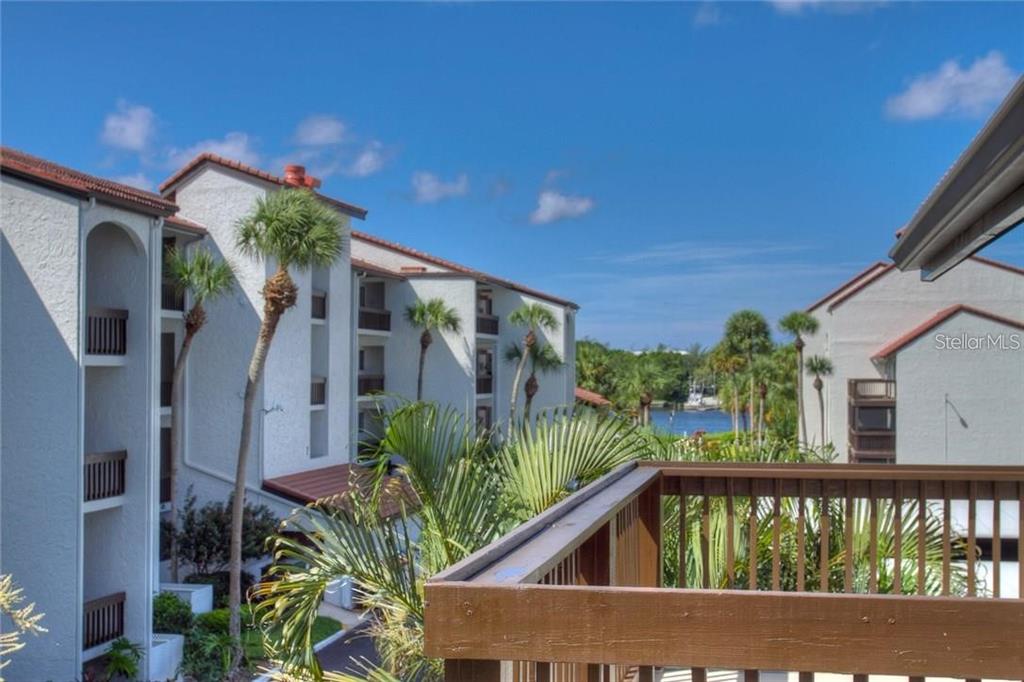 A view from a wooden balcony overlooking a courtyard with palm trees and a waterway — 1622 STICKNEY POINT ROAD UNIT 22-202, SARASOTA, FL