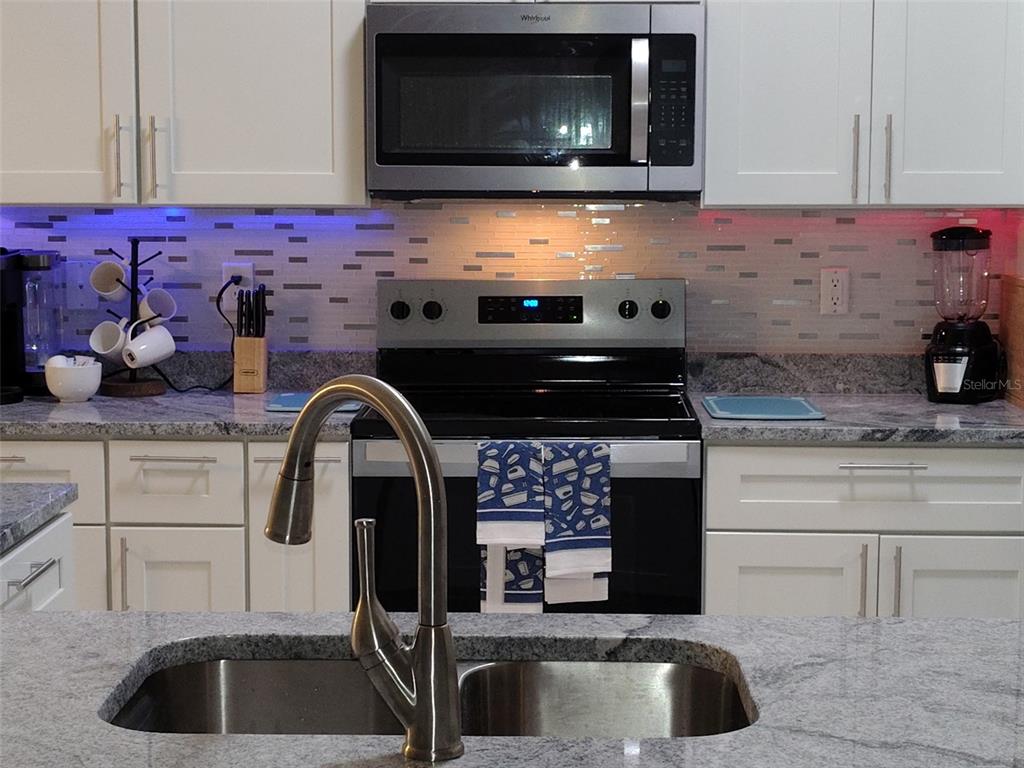 A kitchen features white cabinets, granite countertops, a stainless steel stove, and a microwave — 3985 SE 138TH PLACE, SUMMERFIELD, FL