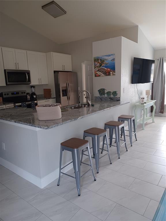 A kitchen features white cabinets, granite countertops, a breakfast bar with four stools, and tile flooring — 3985 SE 138TH PLACE, SUMMERFIELD, FL