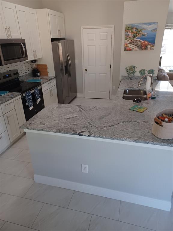 A kitchen features white cabinets, stainless steel appliances, and a granite-topped peninsula — 3985 SE 138TH PLACE, SUMMERFIELD, FL