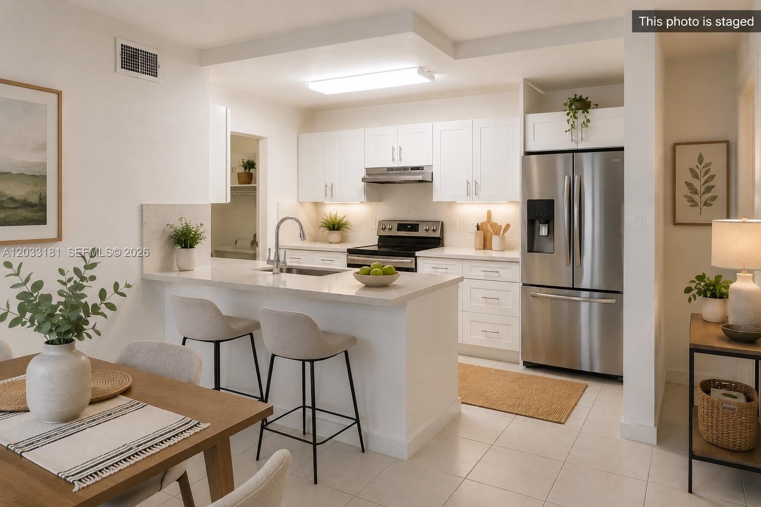A staged kitchen features white cabinets, stainless steel appliances, and a breakfast bar with stools — 240 W Park Dr # 4, Miami FL 33172, MIAMI, FL