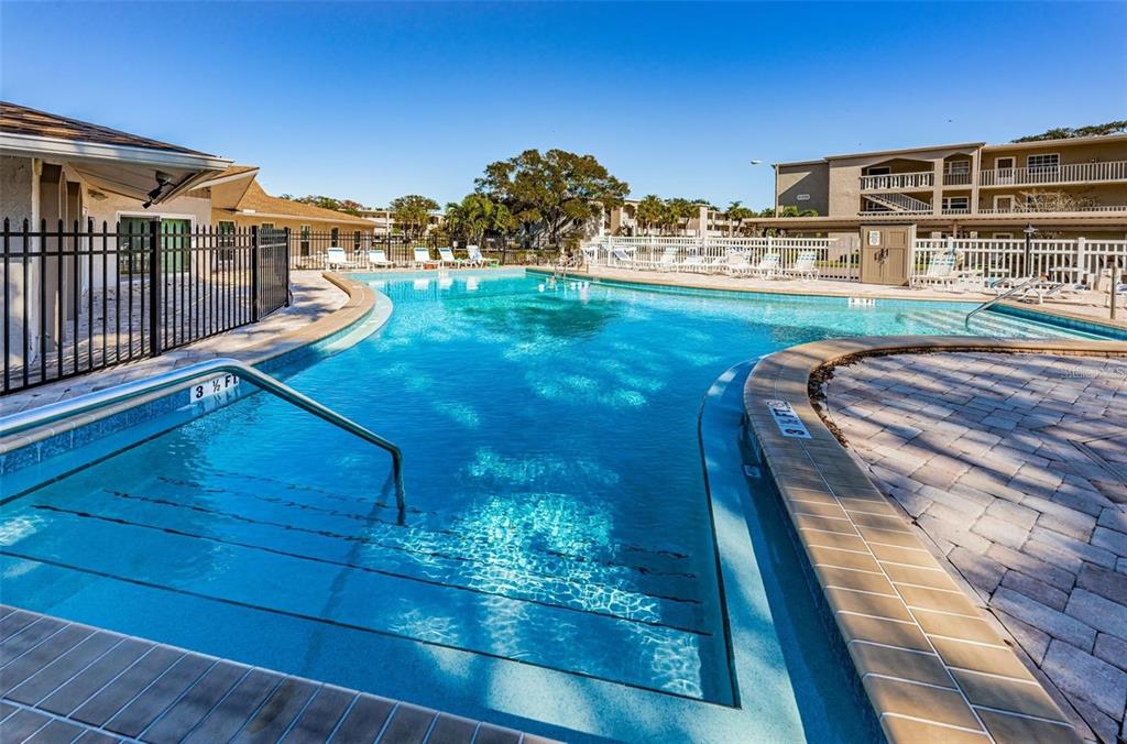 An outdoor swimming pool with steps and a metal handrail surrounded by a paved deck — 841 PATRICIA AVENUE UNIT 103, DUNEDIN, FL