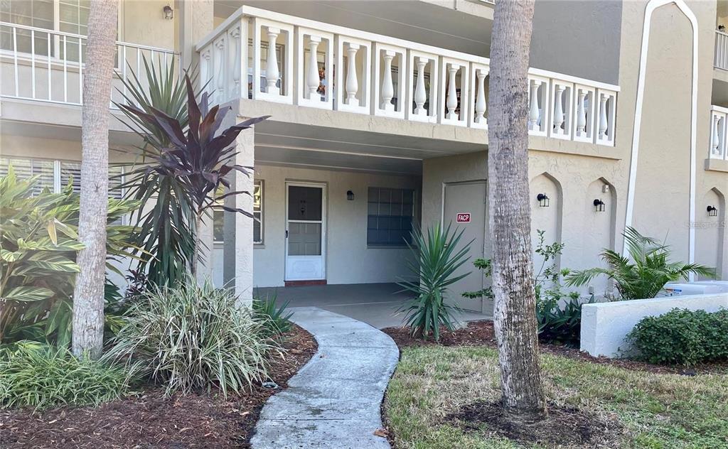 A ground-level building entrance features a concrete walkway, a white door, and a balcony above — 841 PATRICIA AVENUE UNIT 103, DUNEDIN, FL