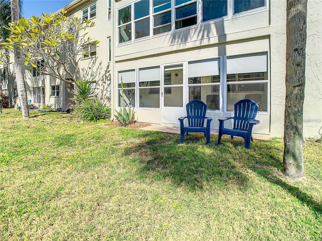 Two blue chairs sit on a small patio outside a screened-in ground floor apartment — 841 PATRICIA AVENUE UNIT 103, DUNEDIN, FL