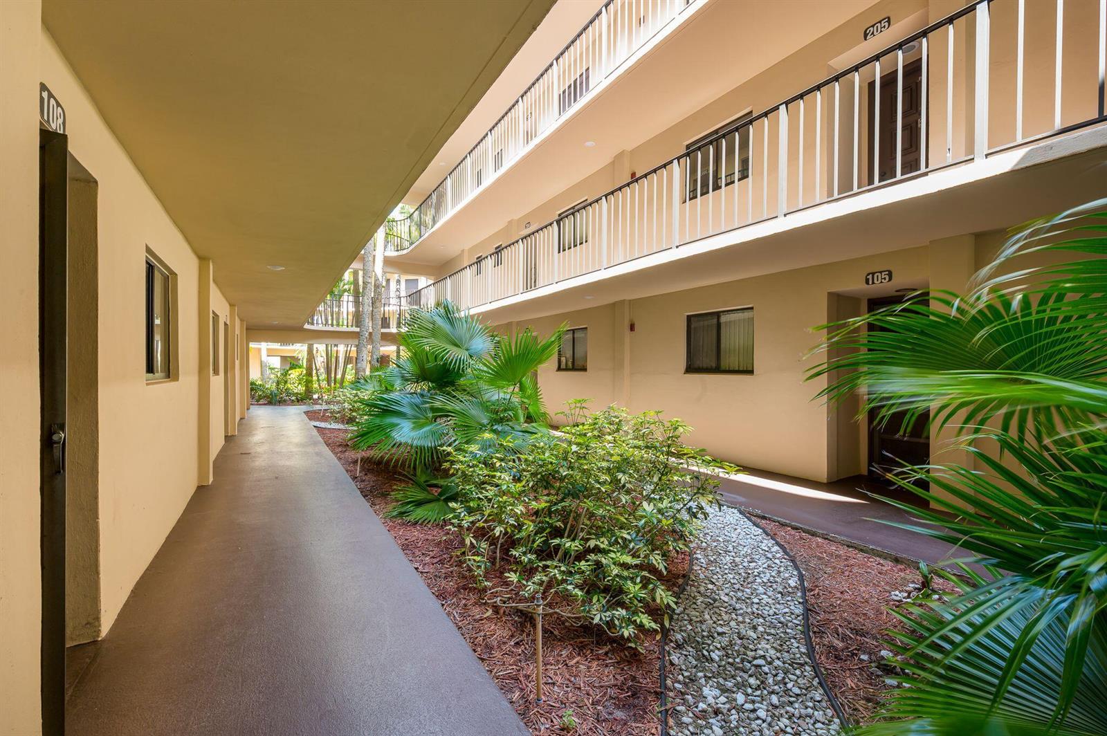 An outdoor walkway leads past a garden area between two levels of apartment building units — 5220 Las Verdes Circle # 108, Delray Beach FL 33484, DELRAY BEACH, FL