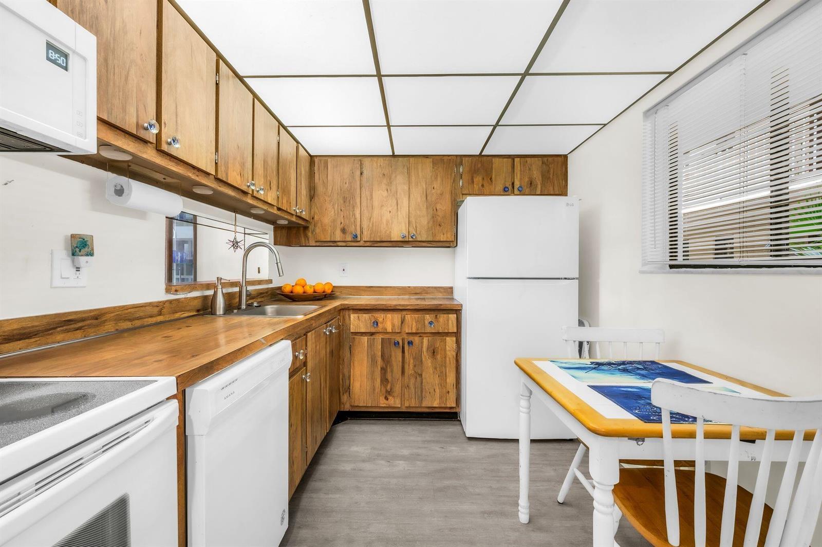 A kitchen features wood cabinets, a white refrigerator, a dishwasher, and a small dining table — 5220 Las Verdes Circle # 108, Delray Beach FL 33484, DELRAY BEACH, FL