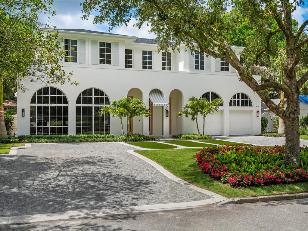 A two-story white house with arched windows and a paved driveway sits behind a garden — 1836 WHITEHALL DRIVE, WINTER PARK, FL