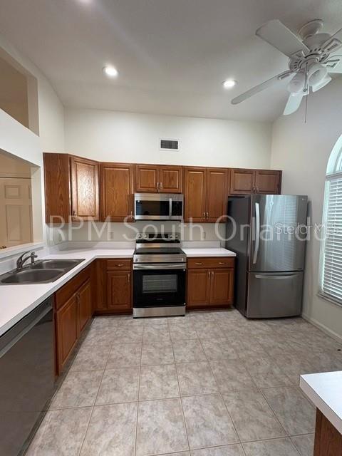 A kitchen features wood cabinets, stainless steel appliances, and tile flooring under a ceiling fan — 1930 TEABERRY COURT, ORLANDO, FL